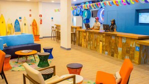 A reception area with a wooden reception desk, blue walls, surfboards on display, and colorful chairs. - Golden Tulip Guarujá (Former Delphin Surf Hotel) (Guarujá)