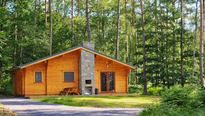 Une cabane en bois avec une cheminée en pierre, une véranda et une allée en gravier, située dans une zone boisée.