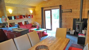Un intérieur de chalet chaleureux comprenant un coin repas, une cuisine avec un poêle à bois et une porte-fenêtre coulissante donnant sur un espace extérieur.