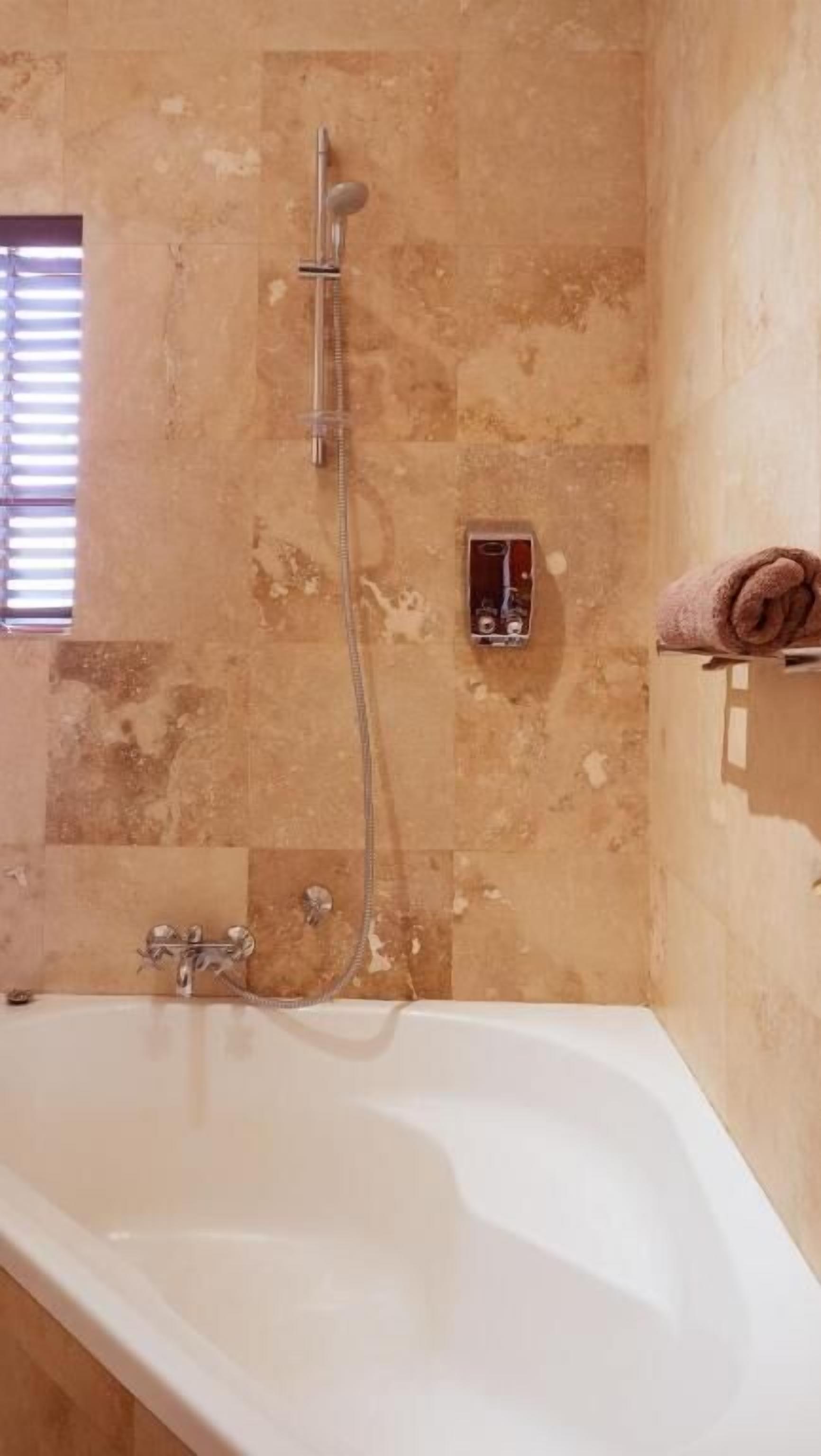A bathroom with a bathtub, a handheld showerhead, and a towel rack.