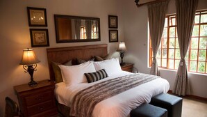 A neatly arranged bedroom with a large bed, bedside tables with lamps, a mirror, and a window with curtains. - Tuareg Guest House (Midrand)