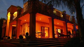A two-story building with a balcony, a stone wall, and outdoor seating. - Tuareg Guest House (Midrand)