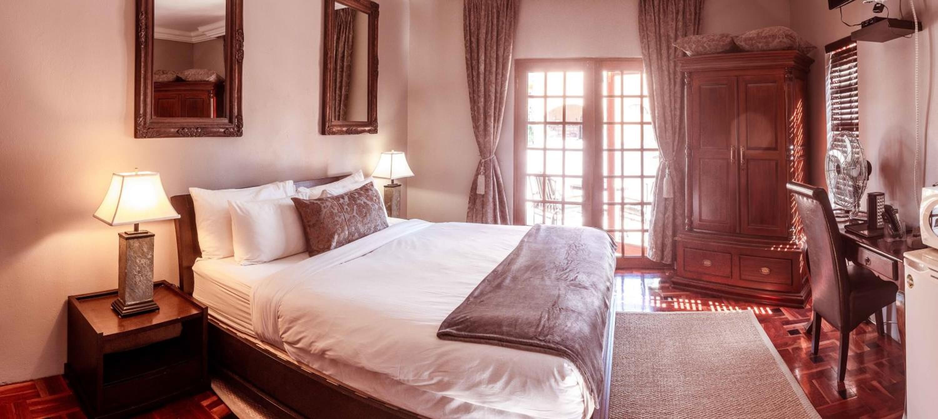 A neatly arranged bedroom with a large bed, two bedside lamps, a wardrobe, and a mirror on the wall.