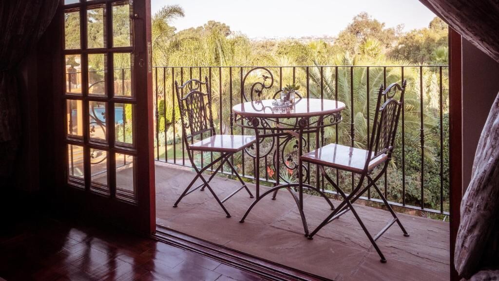 Een open deur die leidt naar een balkon met een tafel en stoelen, omgeven door een metalen hekwerk.