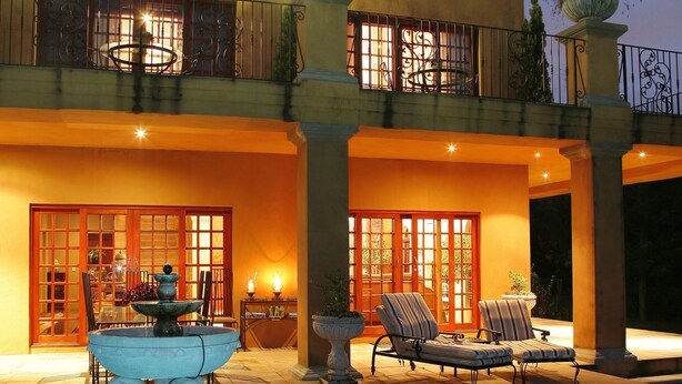 A pool area with a fountain, lounge chairs, and a building with large windows and doors. - Tuareg Guest House (Midrand)