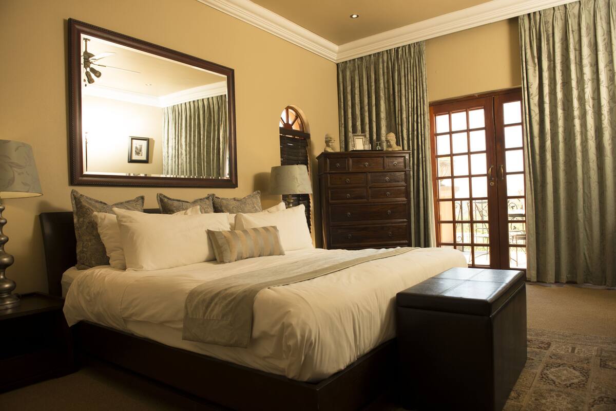 A bedroom with a large bed, a dresser, a mirror, and a window with curtains.