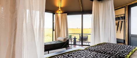 Un dormitorio con una cama grande, un balcón con mesa y sillas, y vistas al paisaje.