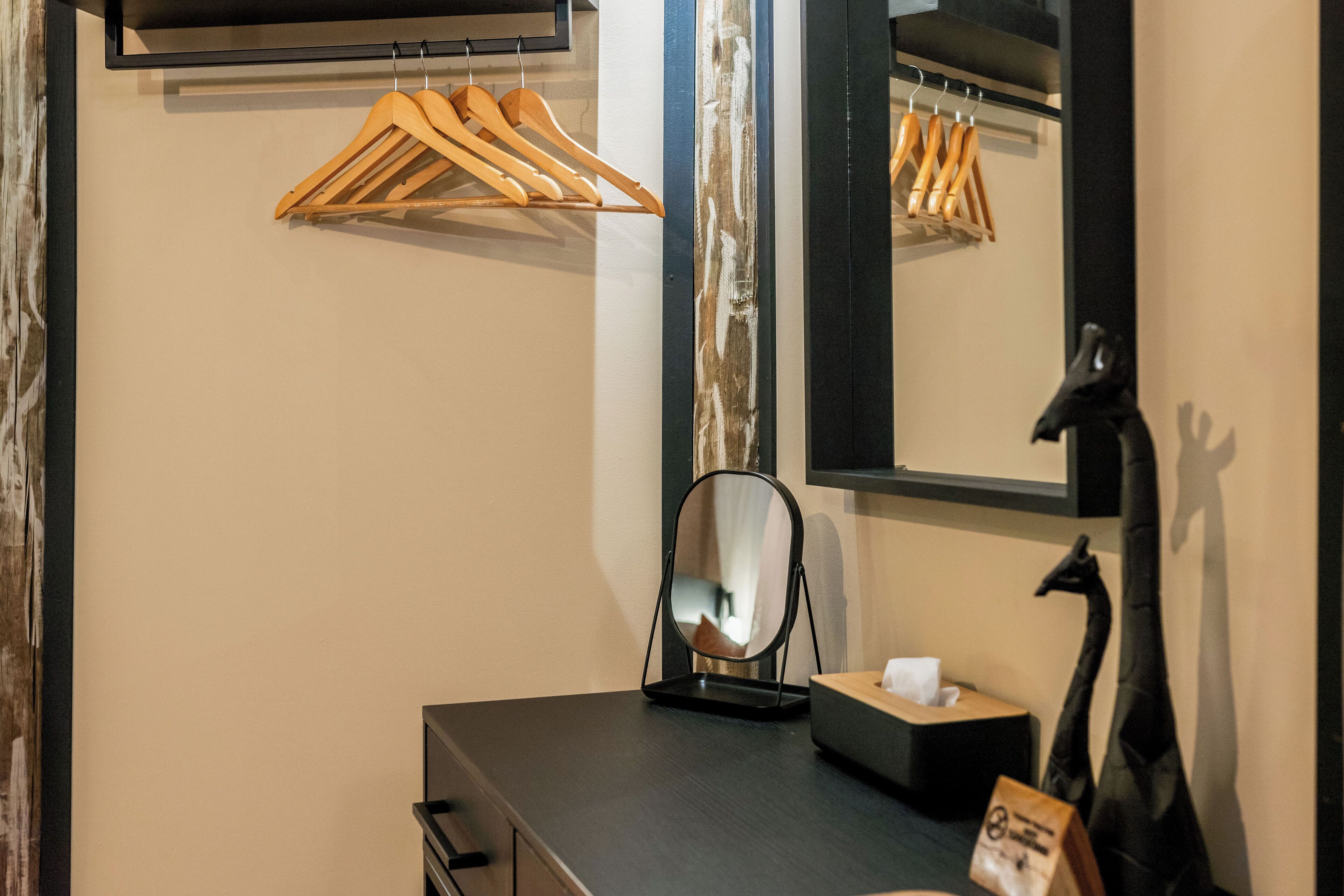 Habitación de hotel con tocador negro, perchero de madera, espejo, escultura negra y una cajita de pañuelos.