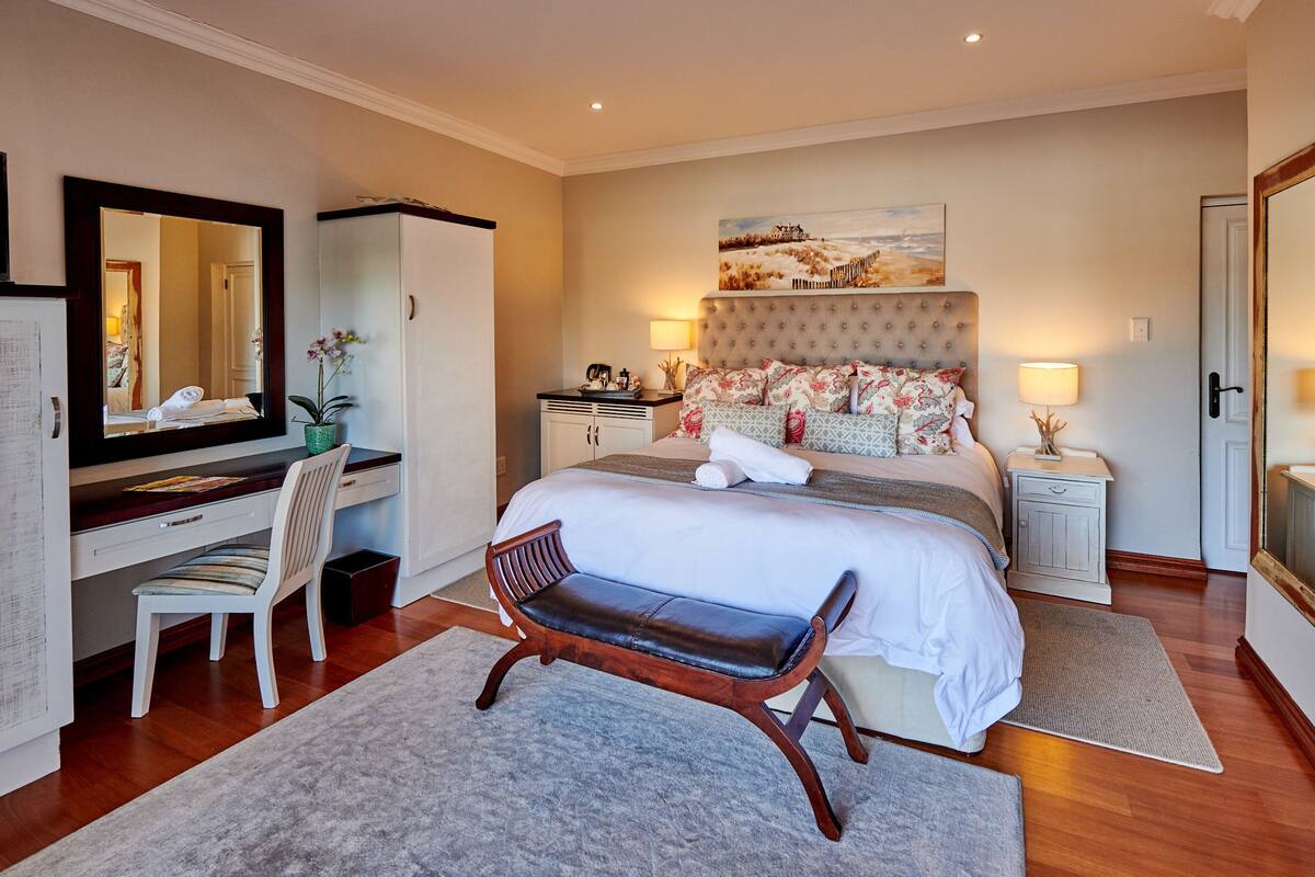 A well-appointed bedroom with a large bed, a desk with a chair, a mirror, and a painting on the wall.