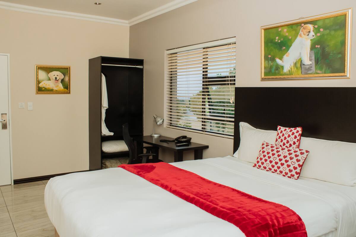 A hotel room with a large bed, a desk, a chair, a wardrobe, and a window with blinds.