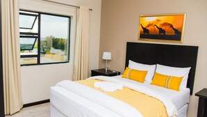 A hotel room with a large bed, a nightstand, a window with curtains, and a painting of giraffes on the wall. - Heavenly Boutique Guesthouse (Johannesburg South)