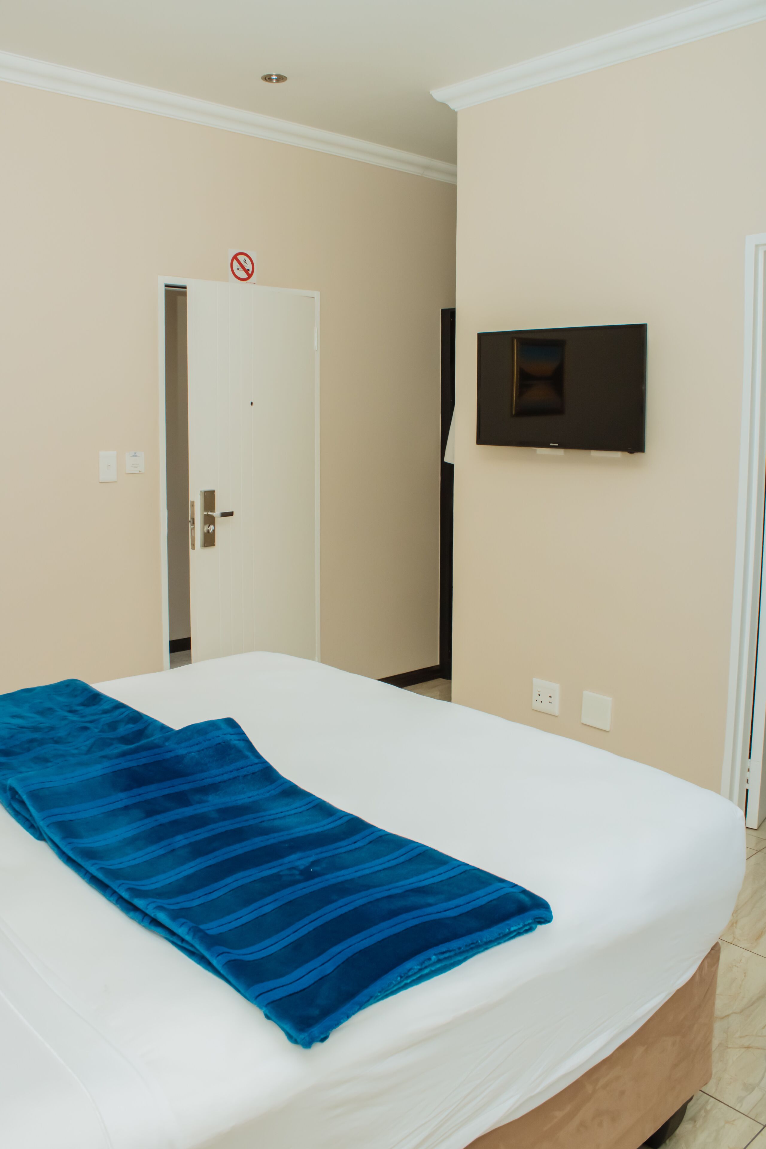 Habitación de hotel con cama, televisor montado en la pared y una puerta con señal de 'no admitidos'.