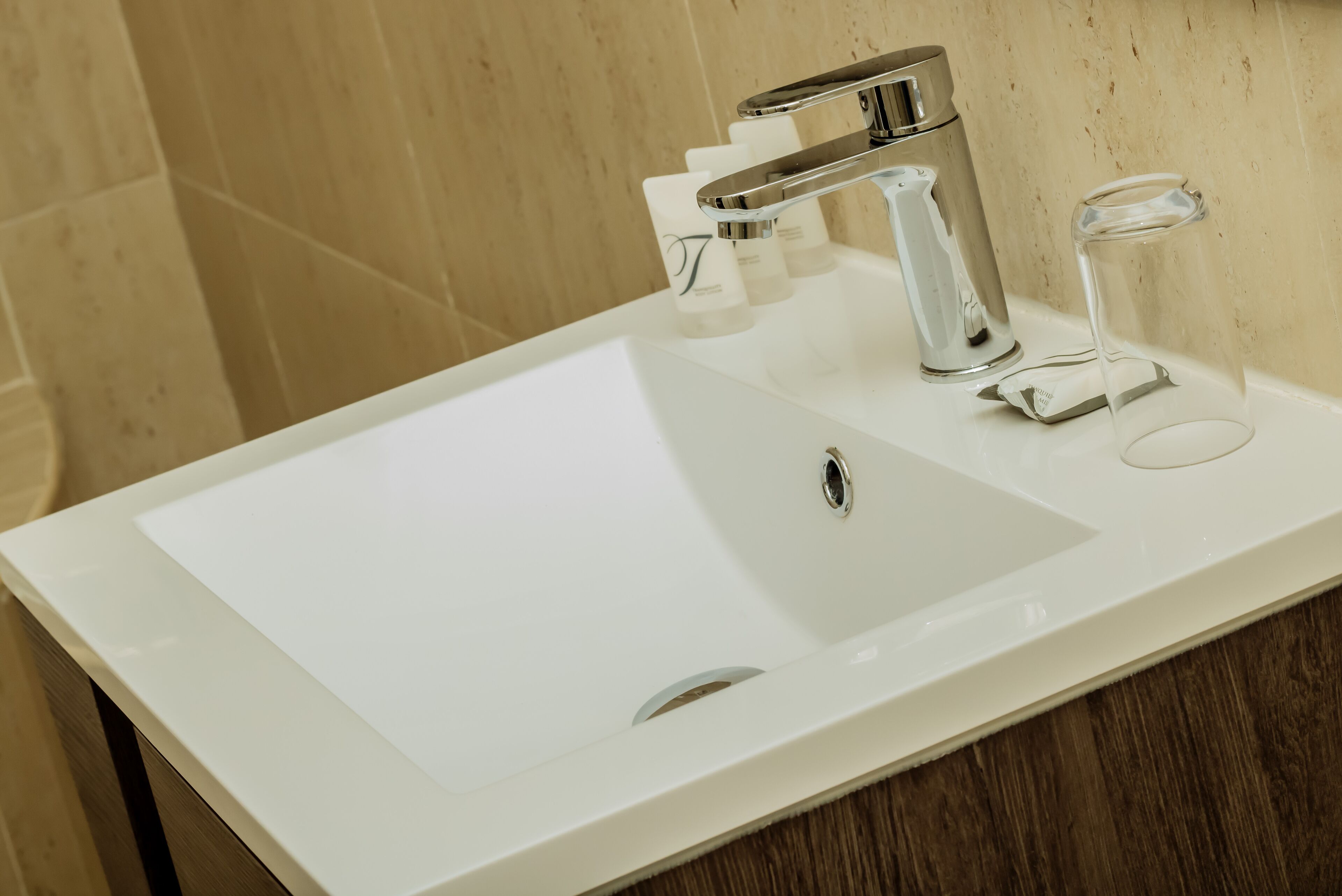 A modern bathroom sink with a chrome faucet, a glass soap dispenser, and a clear glass.