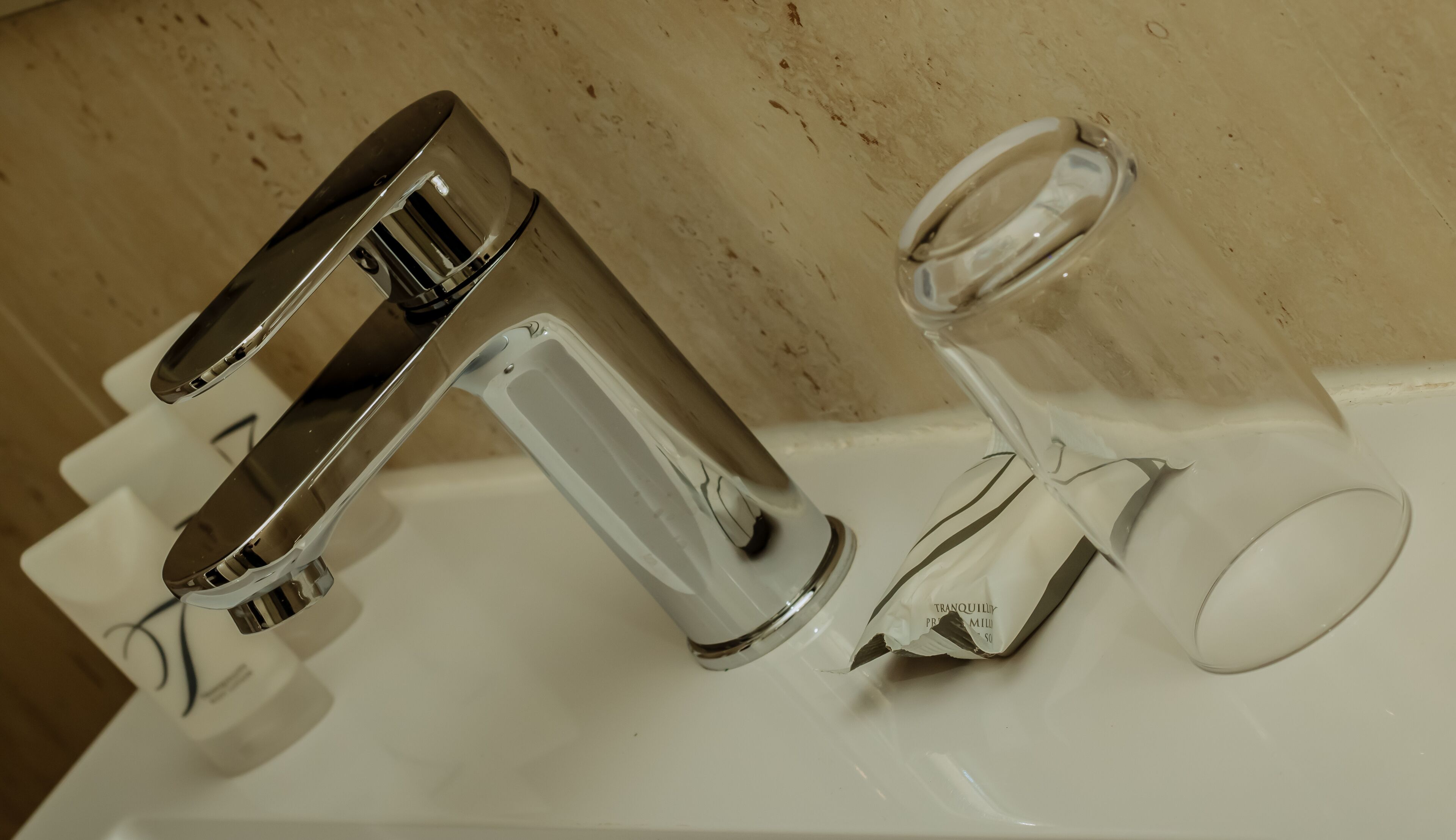 A bathroom sink with a chrome faucet and a clear glass pitcher.