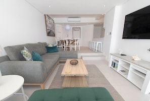 A modern living room with a grey sofa, a wooden coffee table, and a TV mounted on the wall. - 1002 Bermudas (Umhlanga)