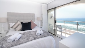 A hotel room with a bed, a bedside table, a nightstand, a window with a view of the ocean, and a balcony with chairs. - 1002 Bermudas (Umhlanga)
