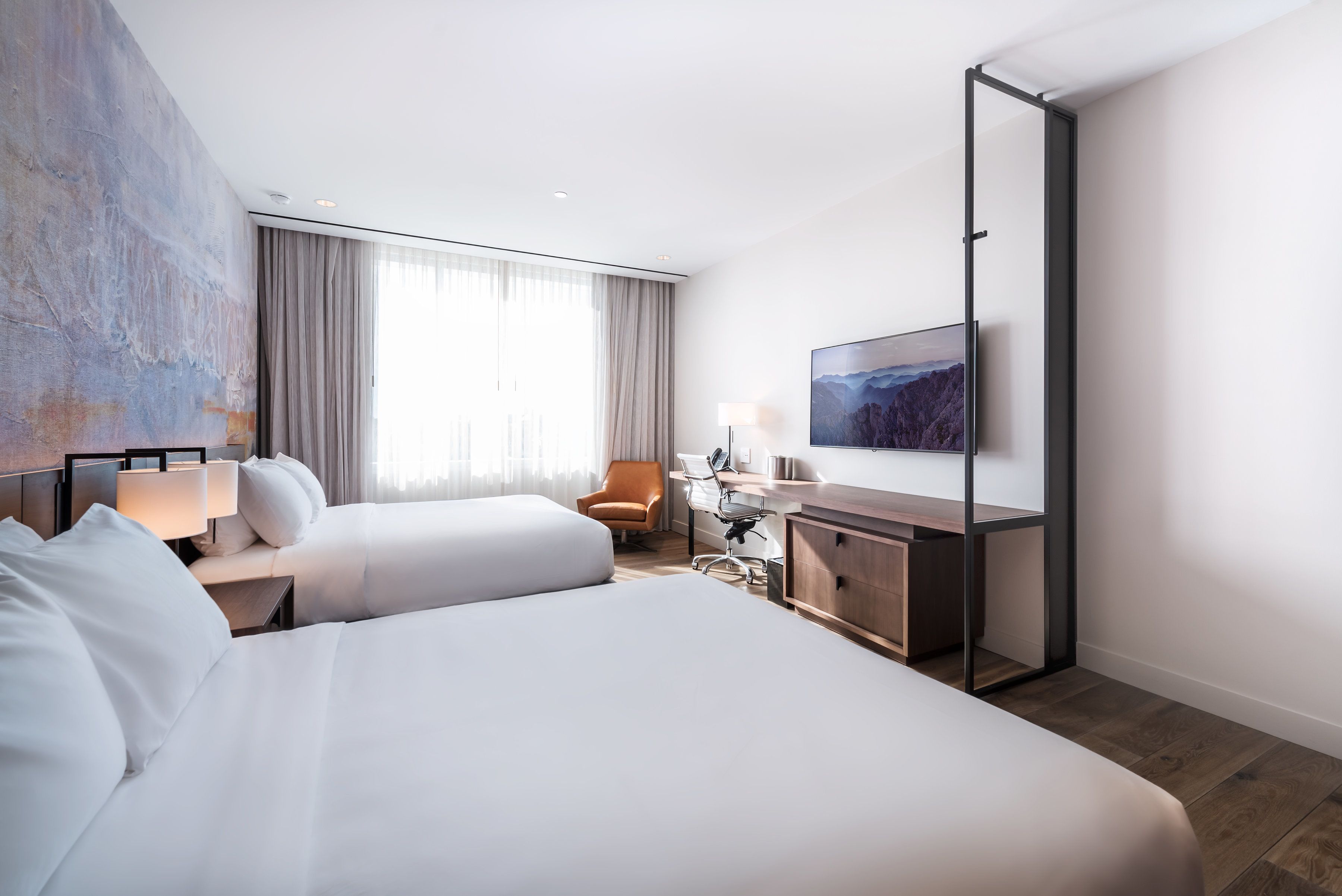 Una habitación de hotel moderna con una cama grande, un escritorio, una silla y un televisor en la pared.