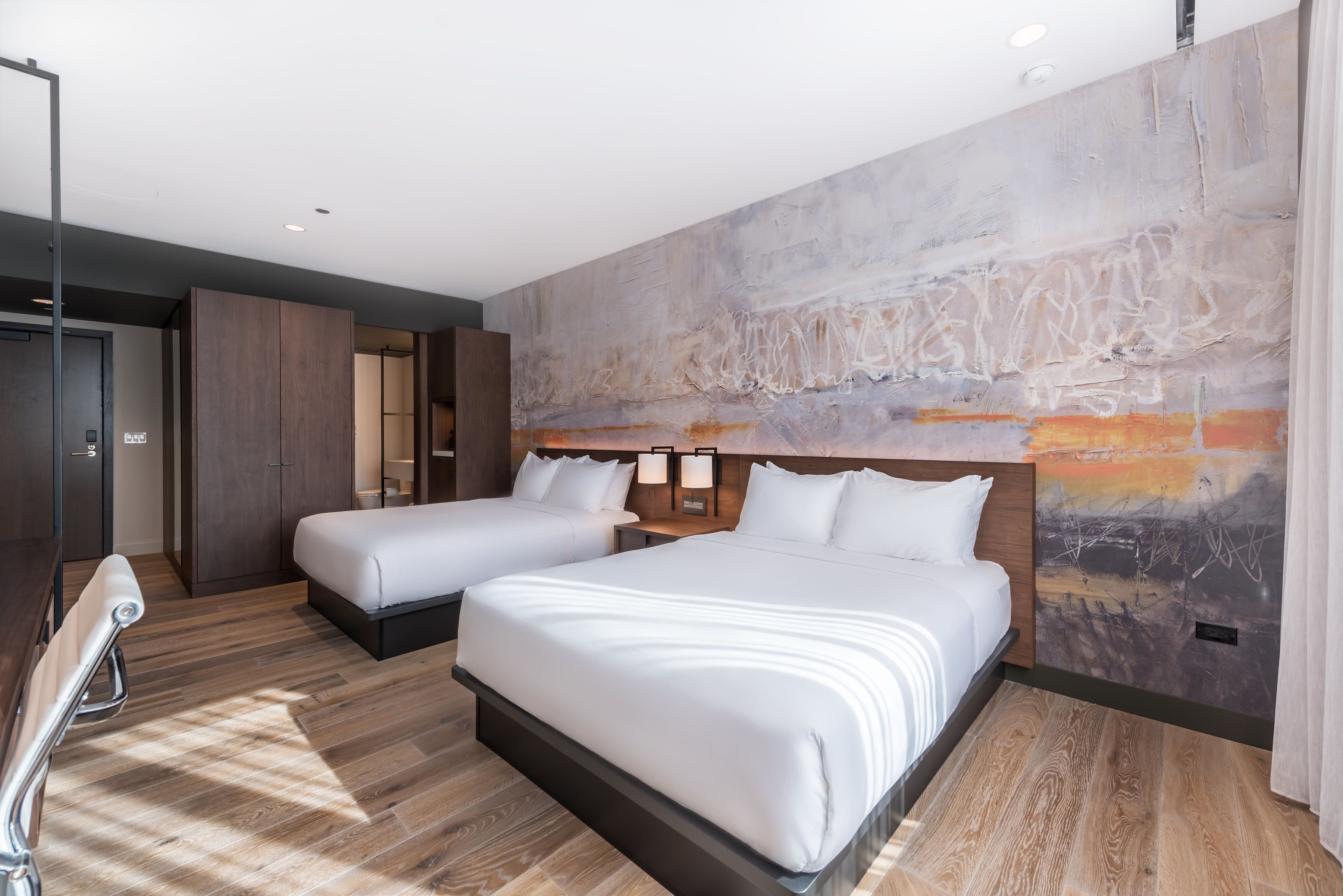 Una habitación de hotel con dos camas, un gran mural abstracto en la pared y suelo de madera.