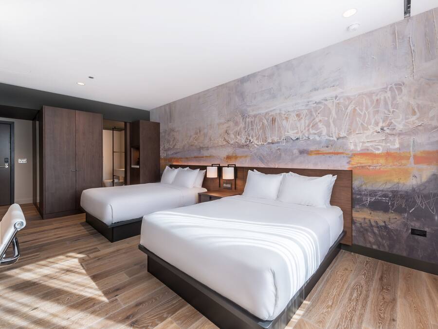 Una habitación de hotel con dos camas, un gran mural abstracto en la pared y suelo de madera.