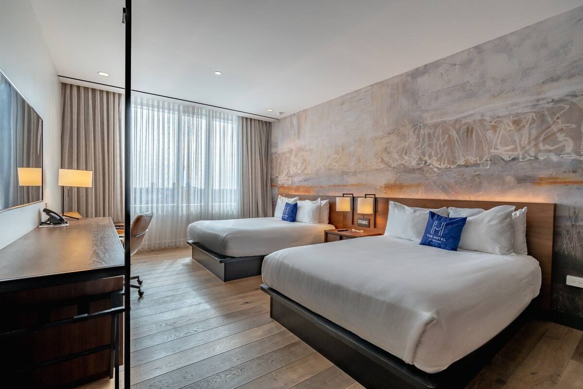 A hotel room with two beds, a desk, and a large window with curtains.