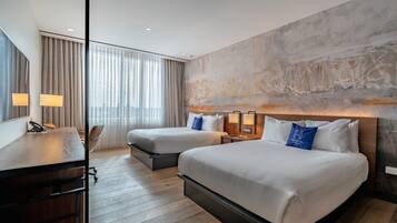 A hotel room with two beds, a desk, and a large window with curtains.
