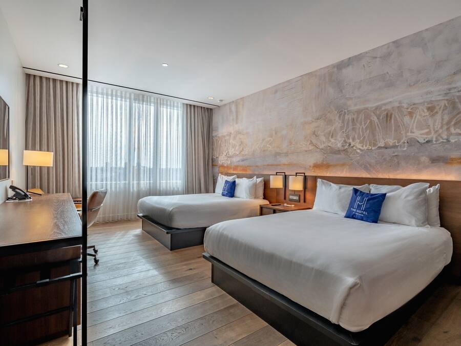A hotel room with two beds, a desk, and a large window with curtains.