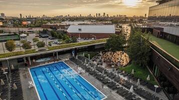 Una piscina con múltiples carriles, asientos exteriores y un horizonte urbano al fondo.