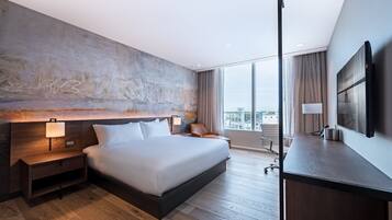 Una habitación de hotel moderna con una cama grande, un escritorio, una silla, un televisor y vista a la ciudad.