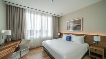 Une chambre d’hôtel avec un grand lit, un bureau avec une chaise, une table de chevet et une fenêtre avec des rideaux.