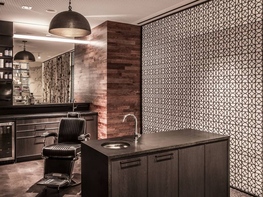 A modern bathroom with a large mirror, a sink, and a chair. There is a decorative wall with a geometric pattern and a wooden panel on the left.