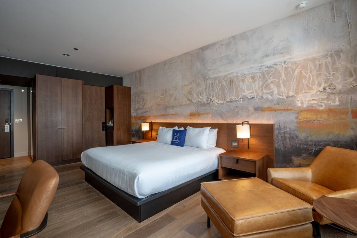 A modern hotel room with a large bed, two bedside tables, a desk, and a chair.