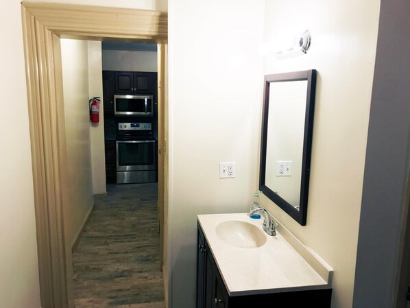 Casa de banho de hotel com lavatório, espelho e vista para a zona da cozinha.