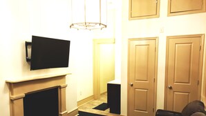 Una sala de estar con chimenea, televisor montado encima, sofá de cuero negro y puerta con un escalón que lleva a otra habitación.
