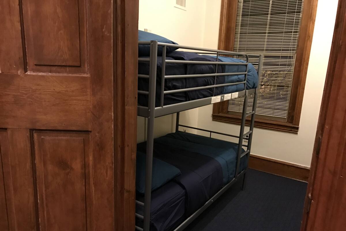 Una cama litera en una habitación con una puerta de madera y una ventana con persianas.