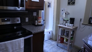 Una cocina equipada con microondas, estufa y cafetera. Hay un cartel en la pared que enumera los utensilios de cocina.