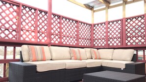 Un área de estar al aire libre cubierta con sofá modular, reposapiés, paneles de celosía roja y un suelo de madera.
