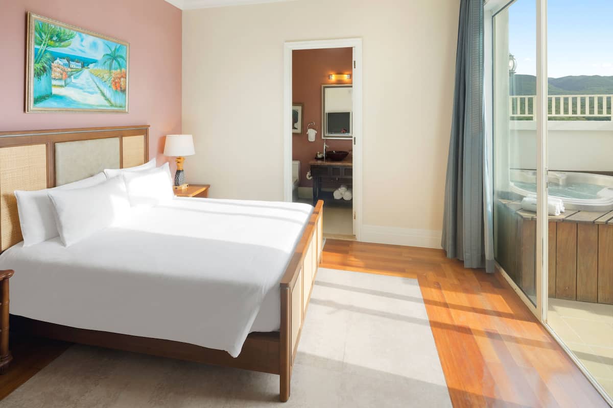 A hotel room with a large bed, a bathroom with a bathtub, and a balcony with a view.