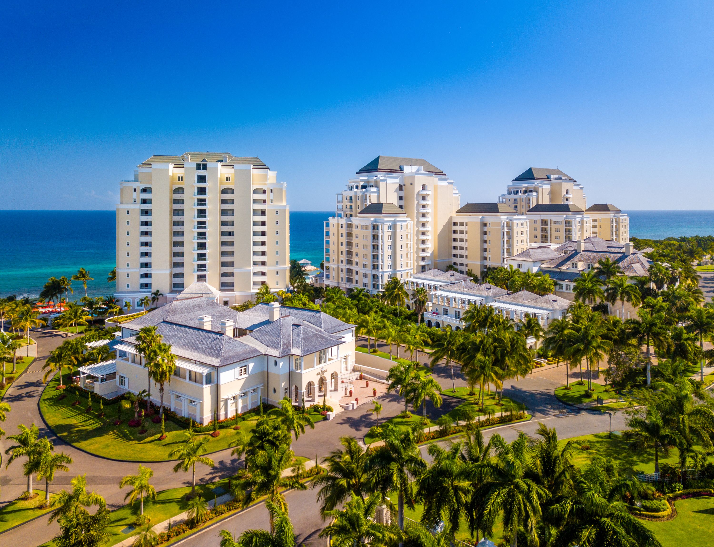 A resort with multiple buildings, a well-maintained lawn, and a view of the ocean.