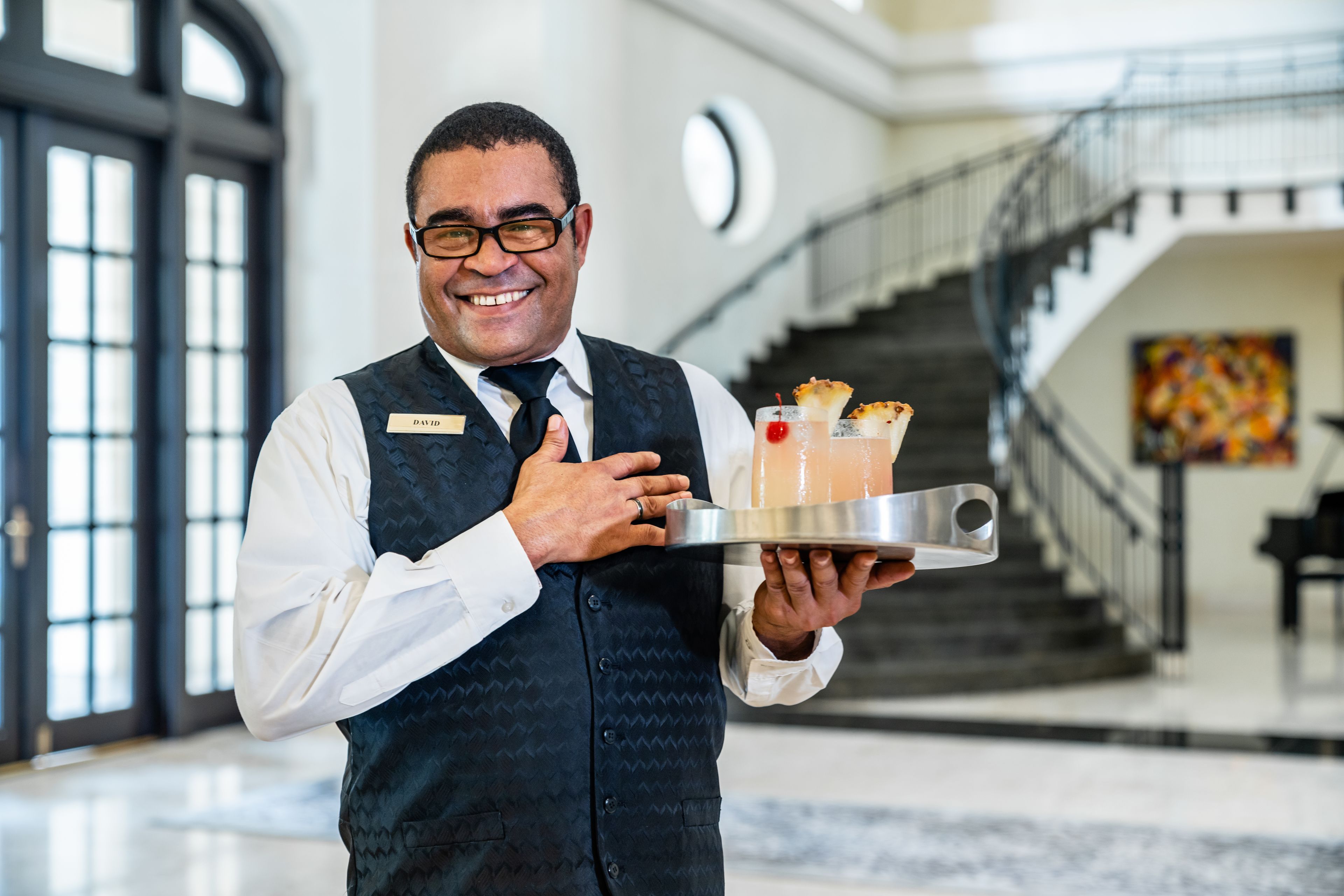 A person in a vest holding a tray with a drink and a dessert.