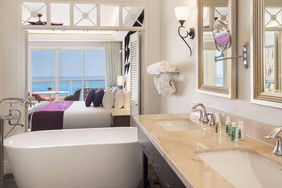 A modern hotel bathroom with a large bathtub, a vanity with multiple sinks, and a large mirror.