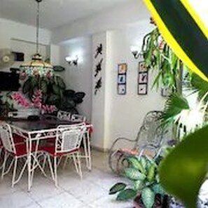 A dining area with a white table and chairs, surrounded by potted plants and wall art. - Dona Amalia (Cienfuegos)