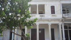A two-story building with a balcony, columns, and a door with a sign. - Dona Amalia (Cienfuegos)