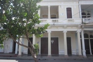 A two-story building with a balcony, columns, and a door with a sign. - Dona Amalia (Cienfuegos)