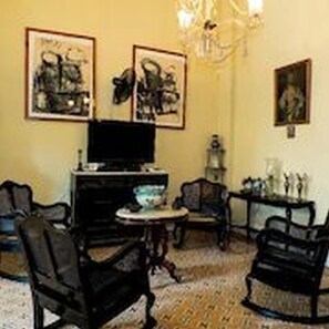 A living room with a television, two framed artworks, a chandelier, and a small round table. - Dona Amalia (Cienfuegos)