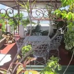 An outdoor patio area with a metal table and chairs, surrounded by greenery and a decorative metal fence. - Dona Amalia (Cienfuegos)