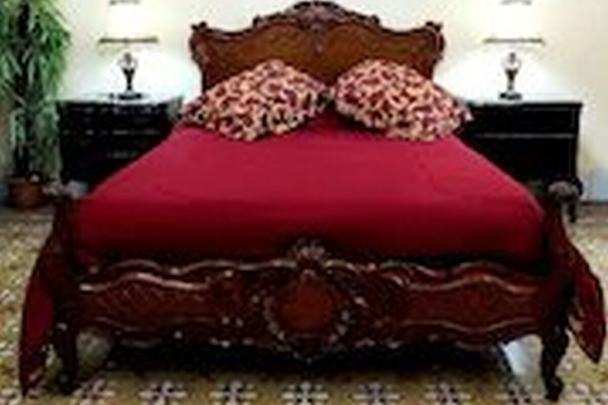 A bed with a red cover, two pillows, and a wooden headboard. There are two bedside tables with lamps.