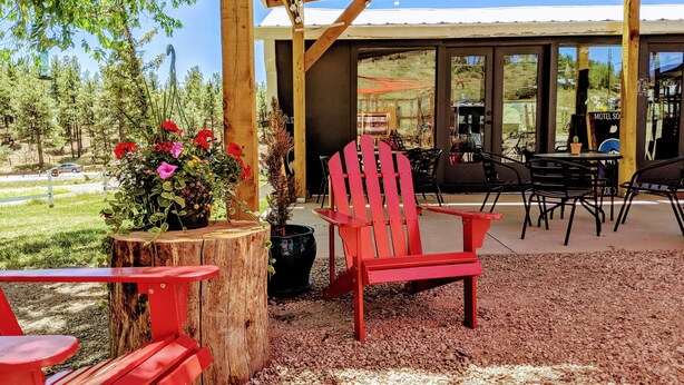 Ein überdachter Außenbereich mit roten Adirondack-Stühlen, einem Holztisch und einem Blumentopf mit roten Blüten.
