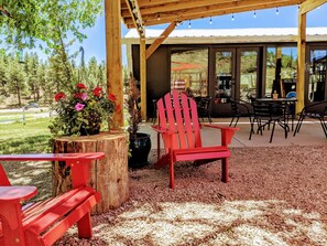 A covered outdoor seating area with red Adirondack chairs, a wooden table, and a potted plant with red flowers. - Motel SOCO (Pagosa Springs)