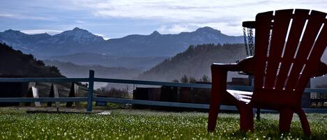 Una silla Adirondack roja en un área con césped, con vistas a montañas y una cerca al frente.