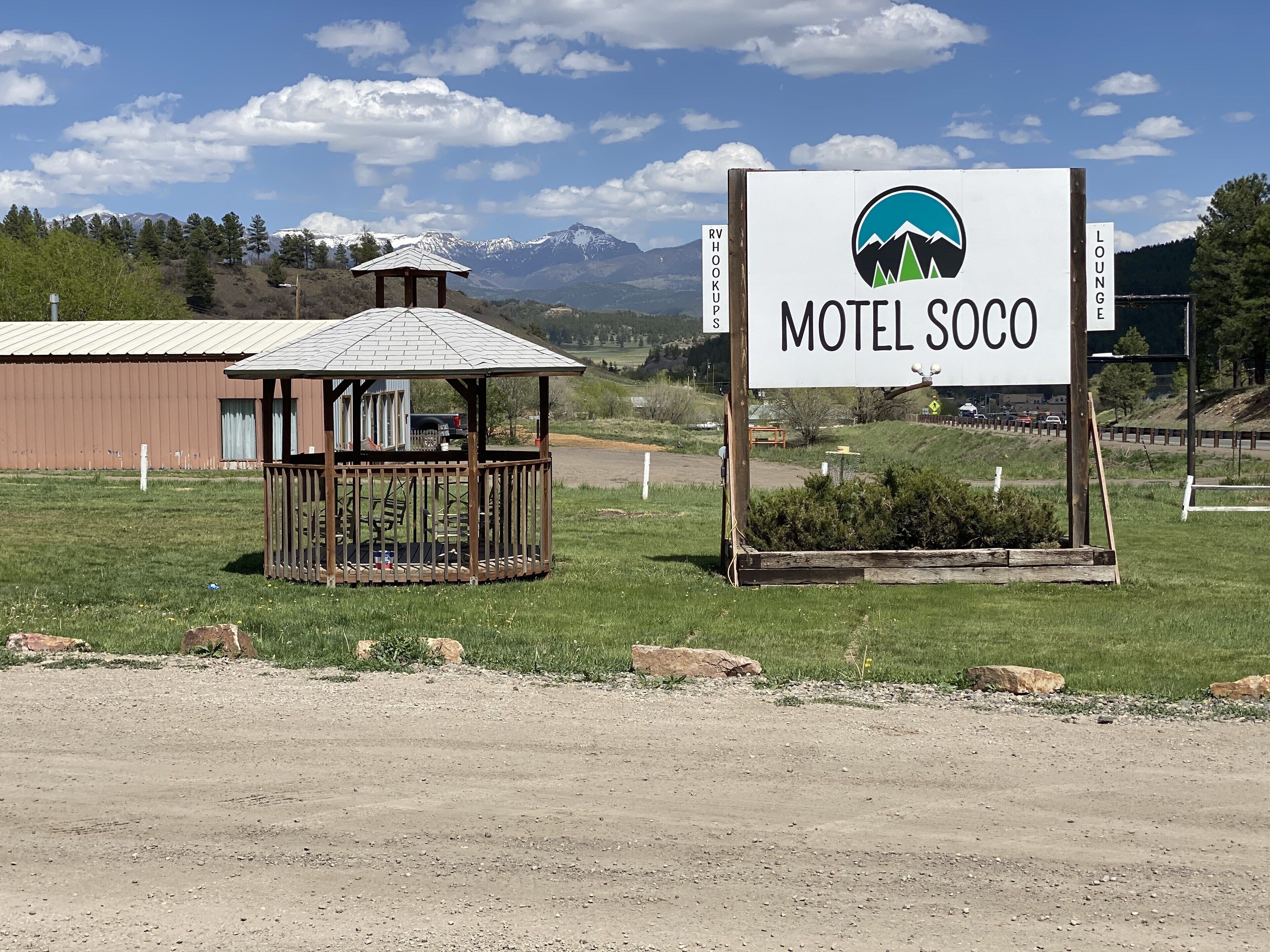 A motel sign with a mountain logo, a small gazebo, and a dirt road in the foreground.